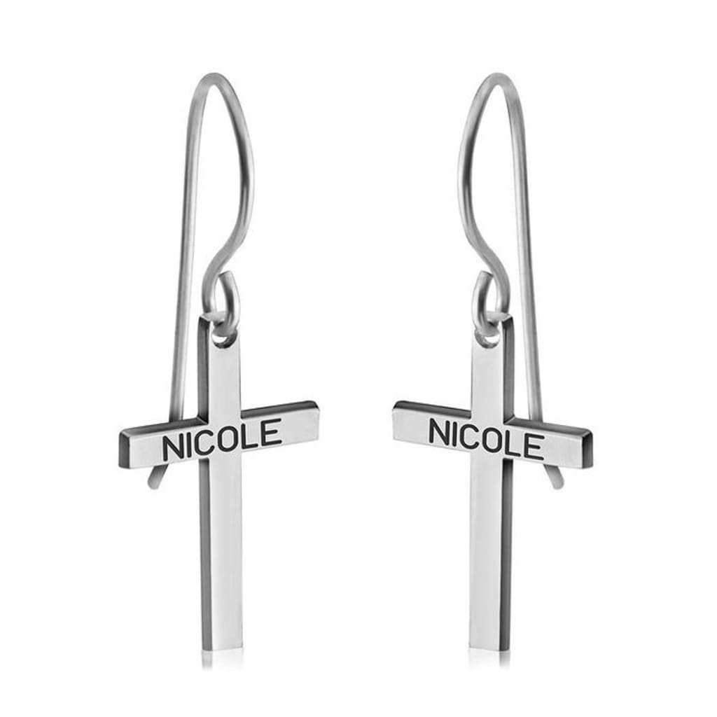 Silver cross-shaped earrings with 'NICOLE' engraving on a white background