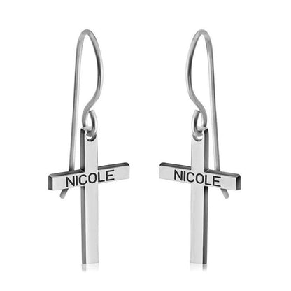 Silver cross-shaped earrings with 'NICOLE' engraving on a white background
