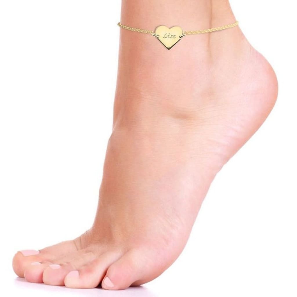 Gold anklet with a heart-shaped charm on a foot against a white background