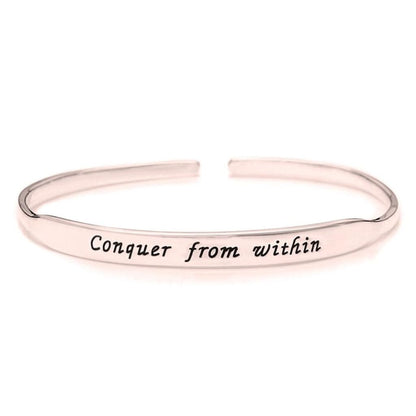 Rose gold bracelet with 'Conquer from within' engraving on a white background