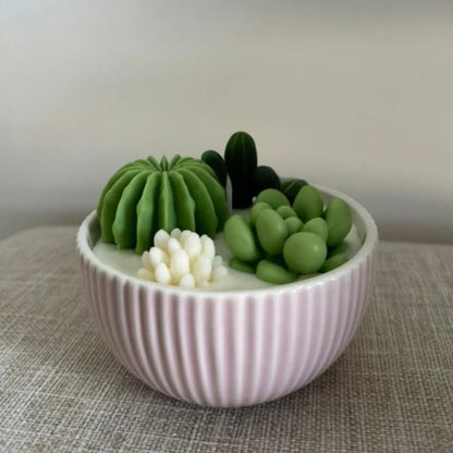 Decorative bowl with green and white cactus-shaped candles on a textured surface.