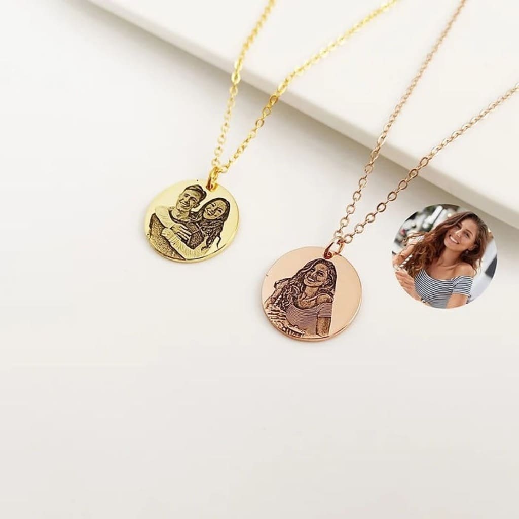 Two gold necklaces with round pendants featuring engraved images on a white surface.