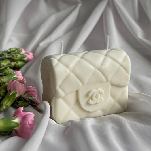 White quilted handbag-shaped candle on a white fabric background with pink flowers.
