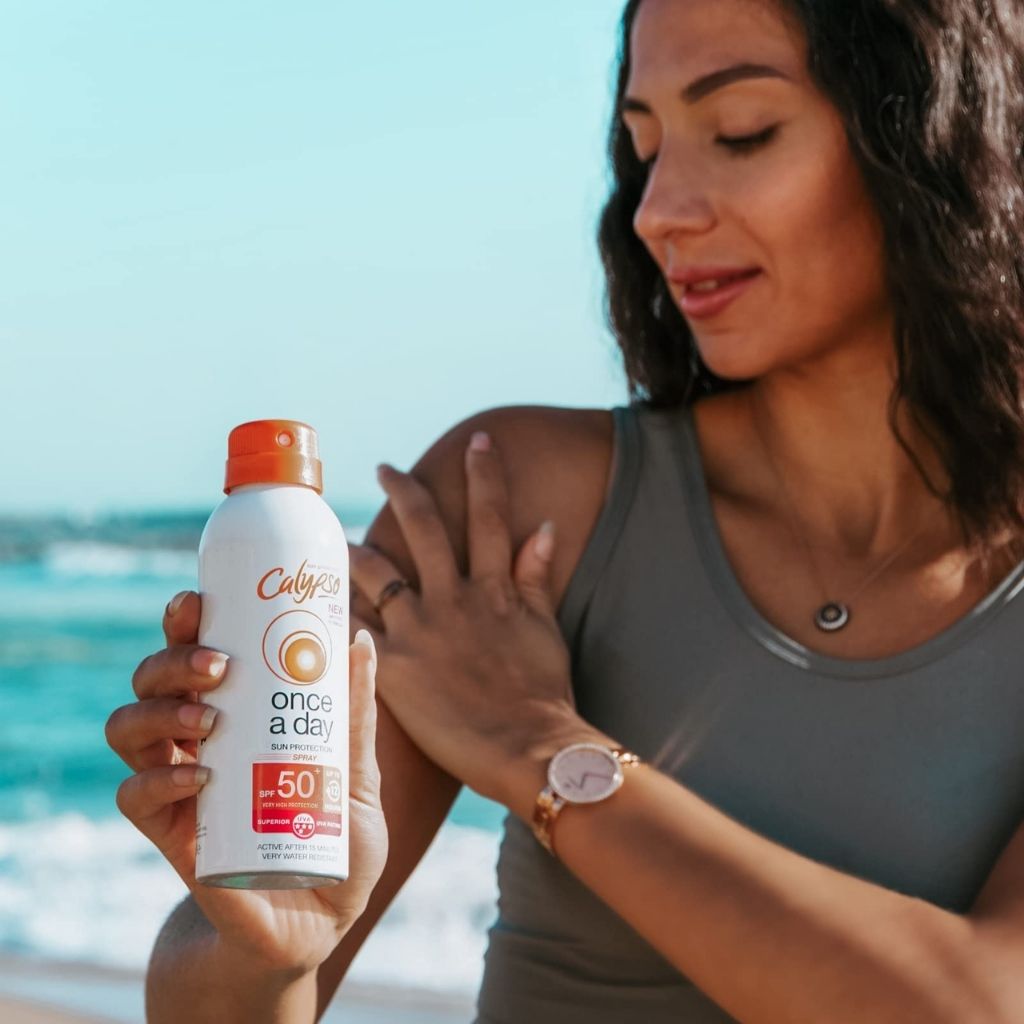 Woman applying sunscreen to her arm with a bottle of Cudy sunscreen at the beach.