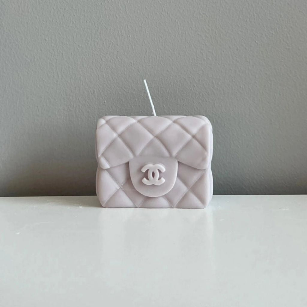 Quilted Chanel bag-shaped candle on a gray surface with a gray background