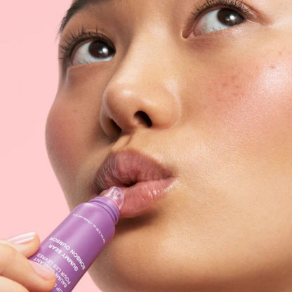Person applying purple lip balm with a pink background