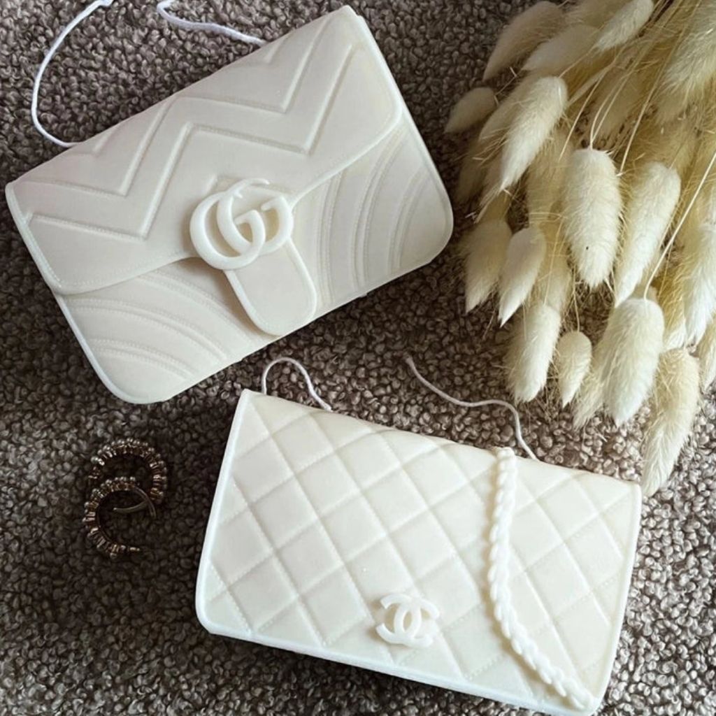 Two white textured handbags with a brand logo on a brown surface with dried plants.