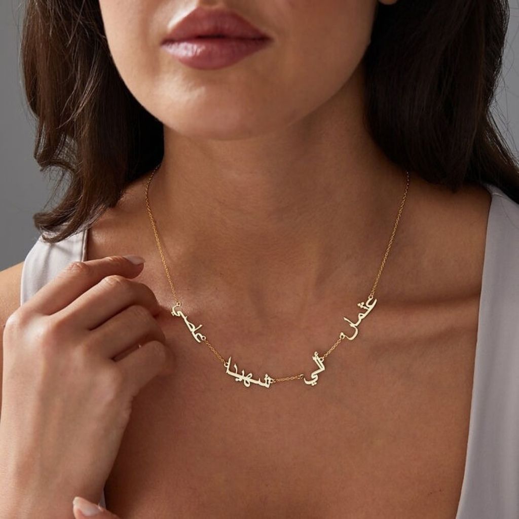 Gold necklace with Arabic script worn by a person against a neutral background