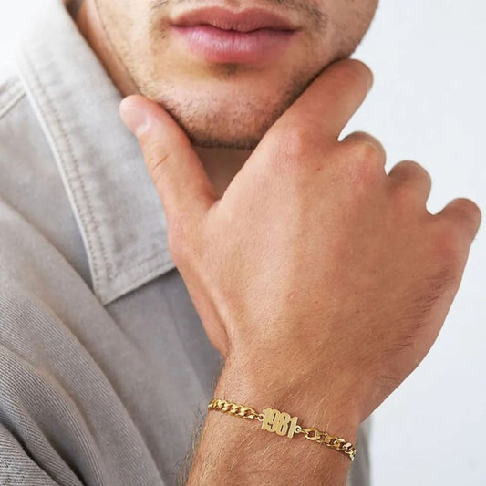 Man wearing a gold bracelet with a visible brand logo on a neutral background