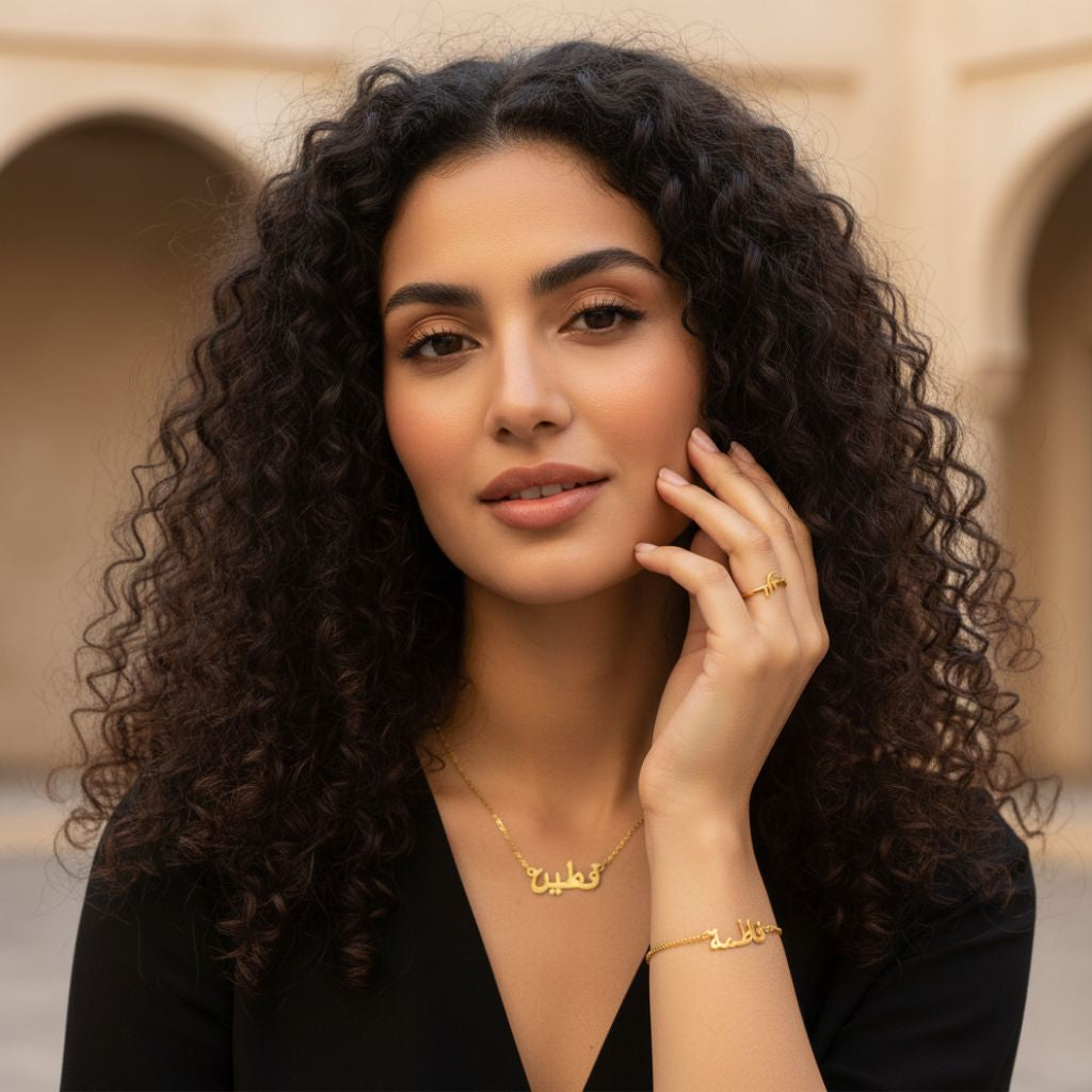 Woman with curly hair wearing gold jewelry in front of a beige wall.