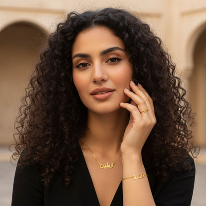 Woman with curly hair wearing gold jewelry in front of a beige wall.