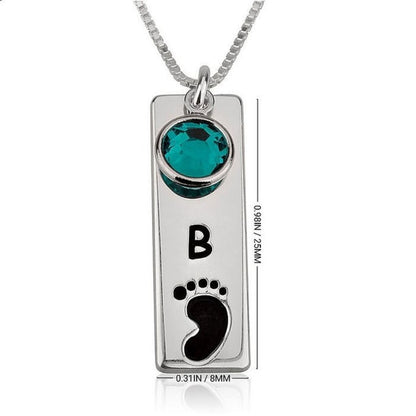 Silver necklace with a green gemstone, black footprint, and letter 'B' on a white background.
