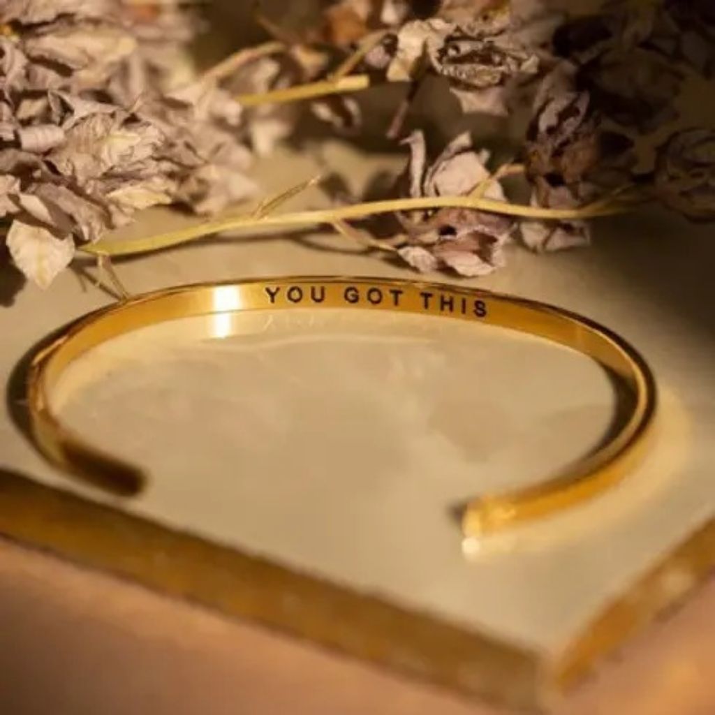 Gold bracelet with 'YOU GOT THIS' text on a light background