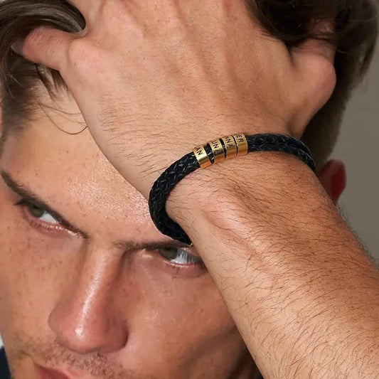 Close-up of a man wearing a black braided bracelet with gold accents on his wrist.