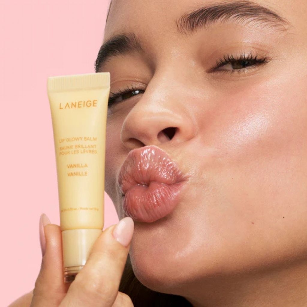 Close-up of a person holding a Laneige lip balm against a pink background