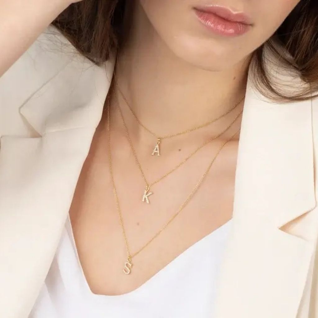 Close-up of a person wearing gold necklaces with letter pendants.