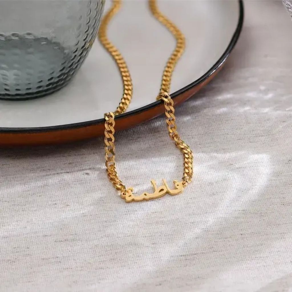 Gold chain necklace with Arabic text on a textured surface