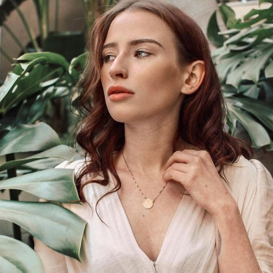 Woman wearing a necklace in front of green plants