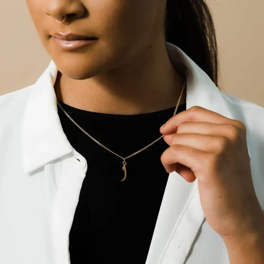 Person wearing a gold necklace with a minimalistic pendant against a neutral background