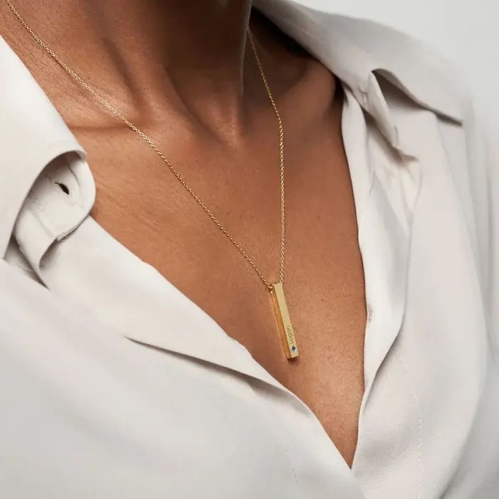Gold necklace with a bar pendant worn by a person in a light-colored shirt.