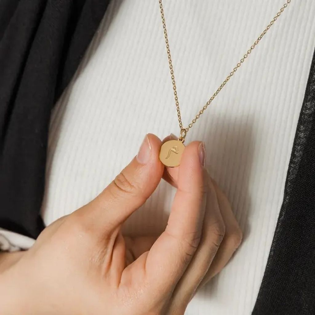 Gold necklace with a round pendant held by a hand against a neutral background