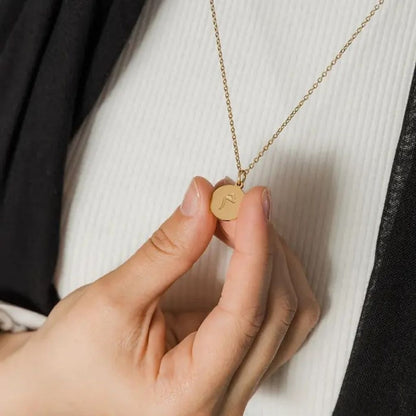 Gold necklace with a round pendant held by a hand against a neutral background