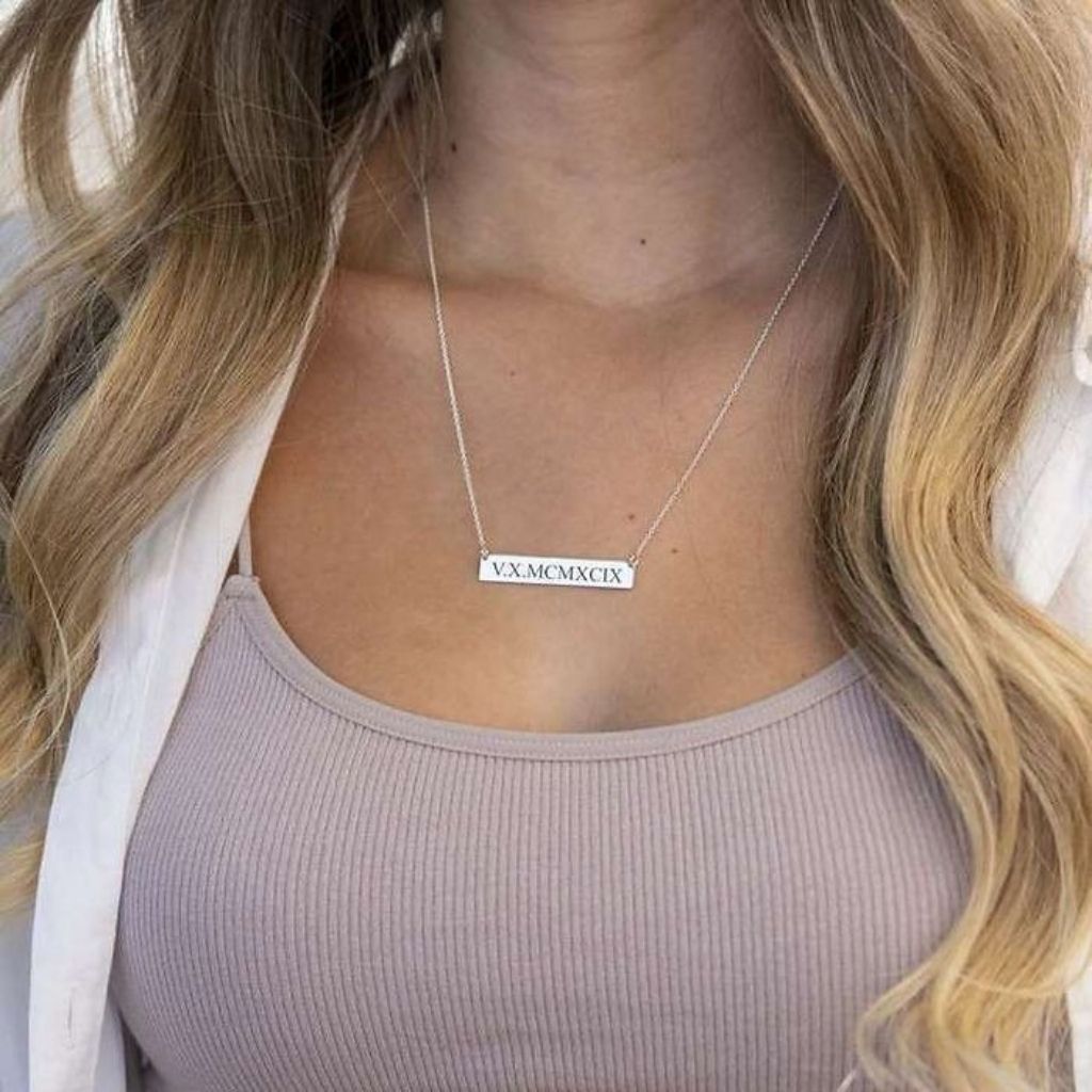Necklace with Roman numeral pendant worn by a person with long blonde hair.