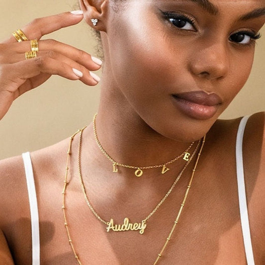Woman wearing gold necklaces with 'Audrey' and 'LOVE' on a beige background