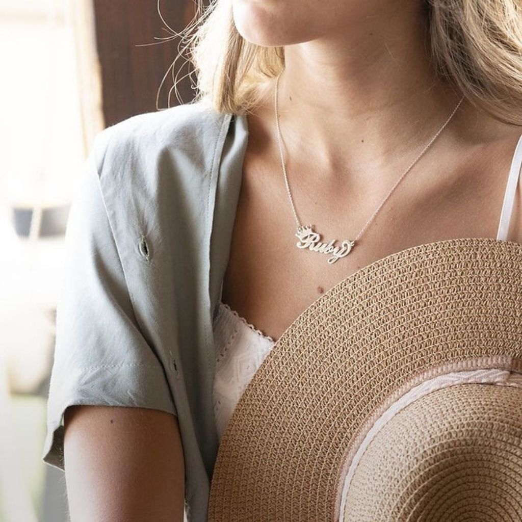 Person wearing a necklace with a 'Riley' pendant, blurred background