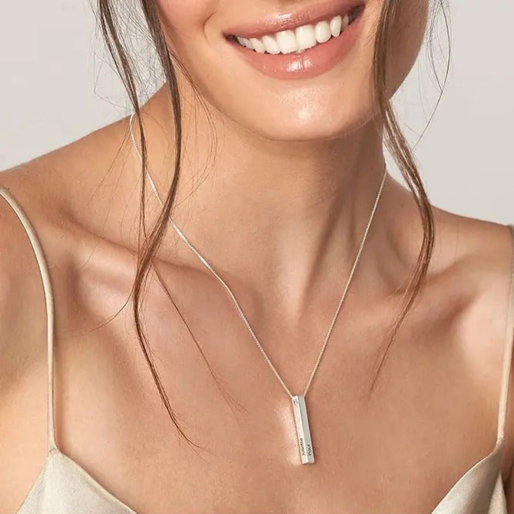 Woman wearing a silver necklace with a bar pendant against a neutral background