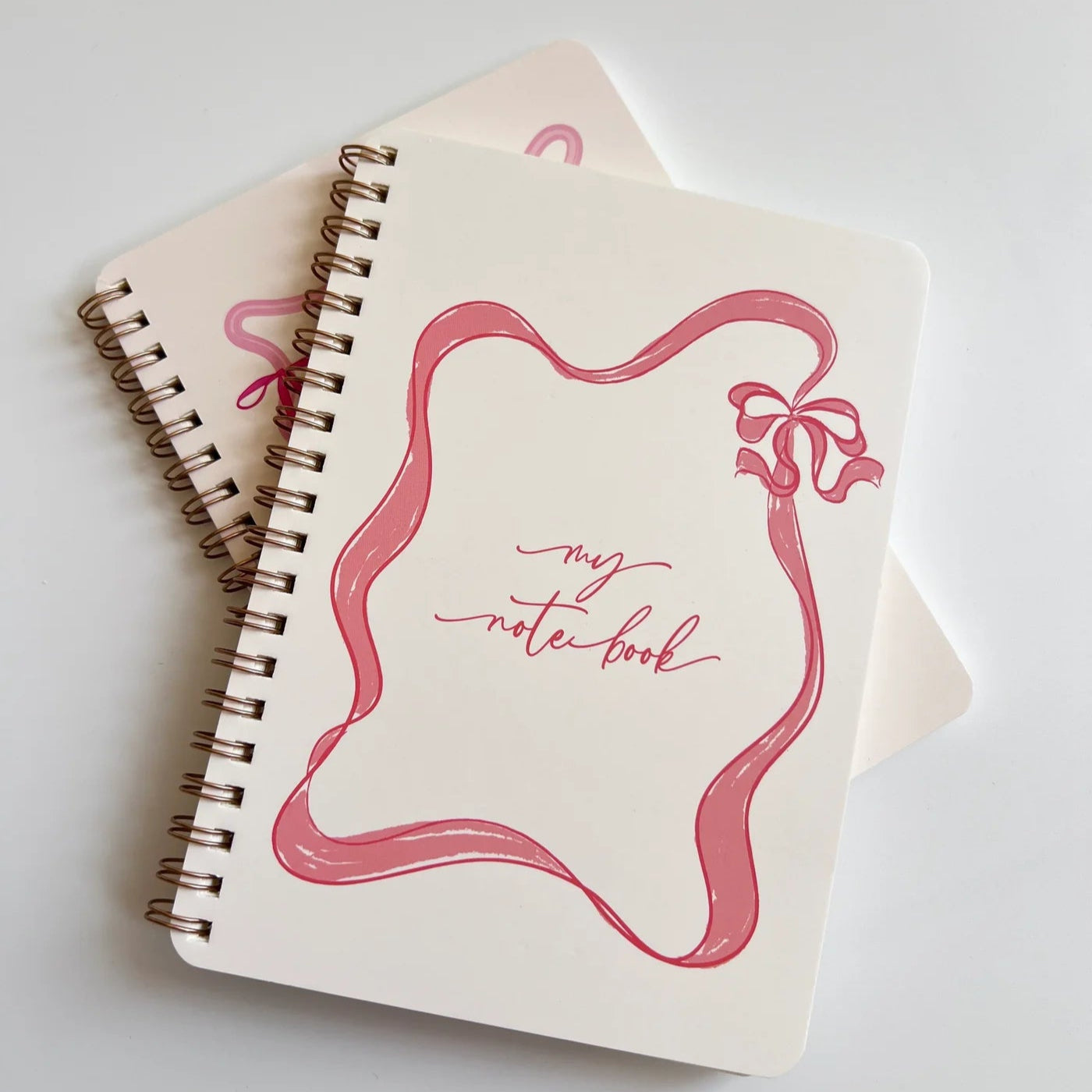 Two spiral-bound notebooks with pink design and text on a light gray background