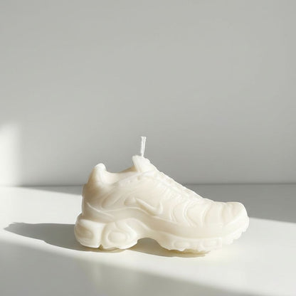 White sneaker-shaped candle on a white surface with a light gray background