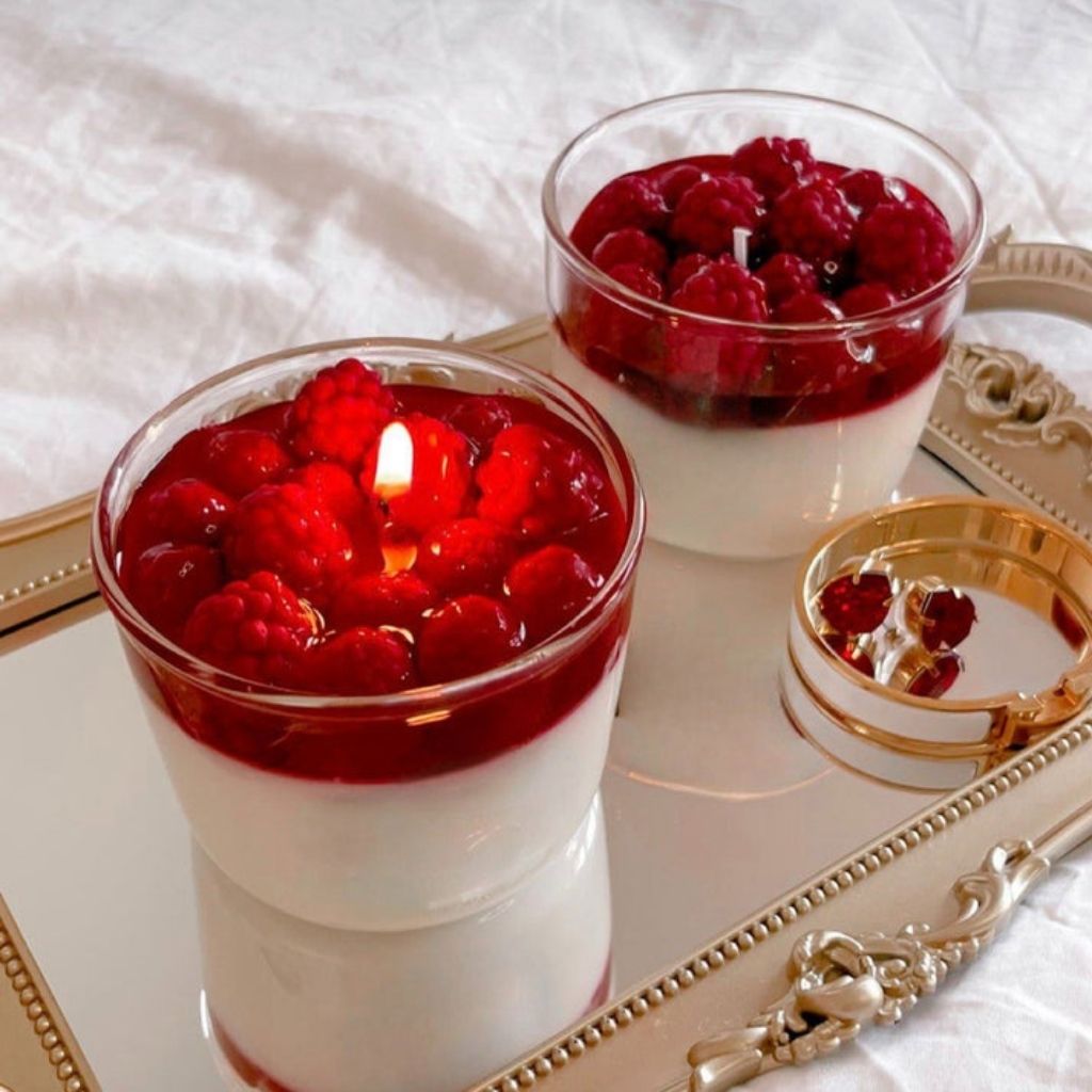 Two glass containers with a dessert topped with raspberries on a decorative tray.
