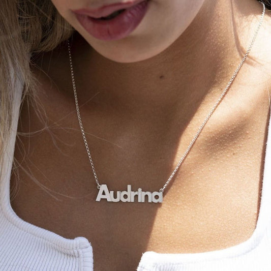 Silver necklace with 'Audrina' pendant on a person wearing a white top.