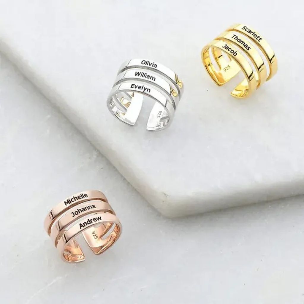 Three personalized name rings in gold, silver, and rose gold on a white surface.