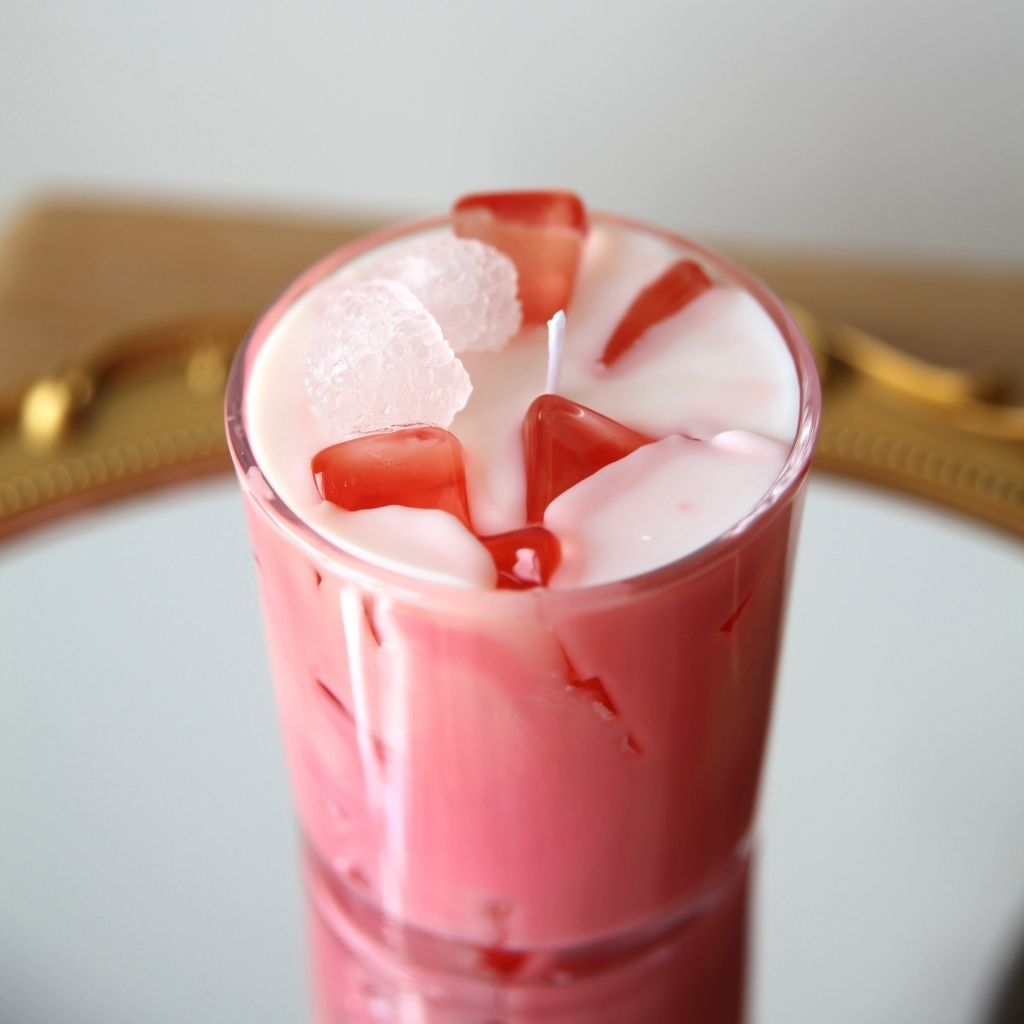 Pink candle with ice cube design in a glass container on a white surface.