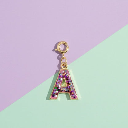 Gold letter 'A' charm with glittery design on a pastel purple and green background