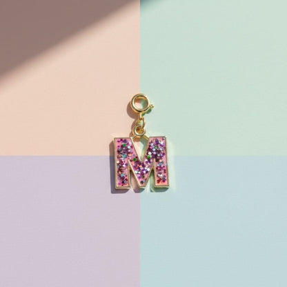 Letter 'M' charm with pink glitter on a pastel background