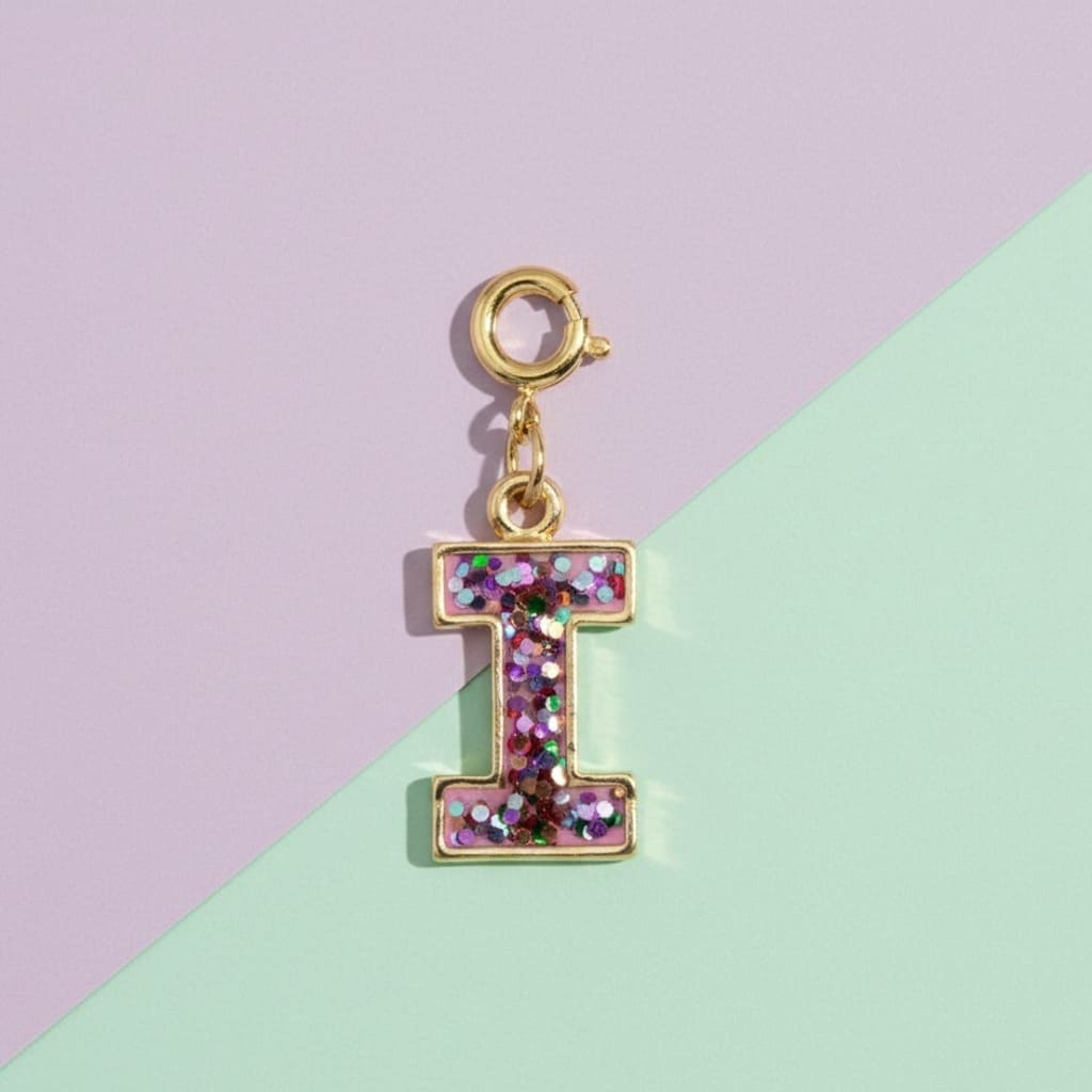 Gold charm with letter 'I' made of glittery material on a two-tone background