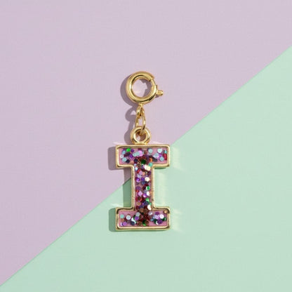 Gold charm with letter 'I' made of glittery material on a two-tone background