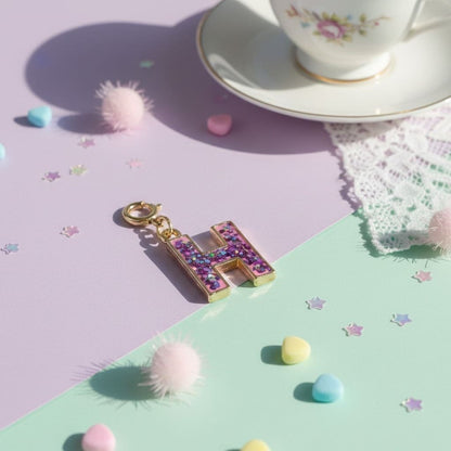 Decorative letter 'H' charm on a colorful surface with a teacup in the background
