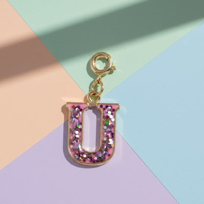 Letter 'U' charm with pink glitter on a colorful geometric background