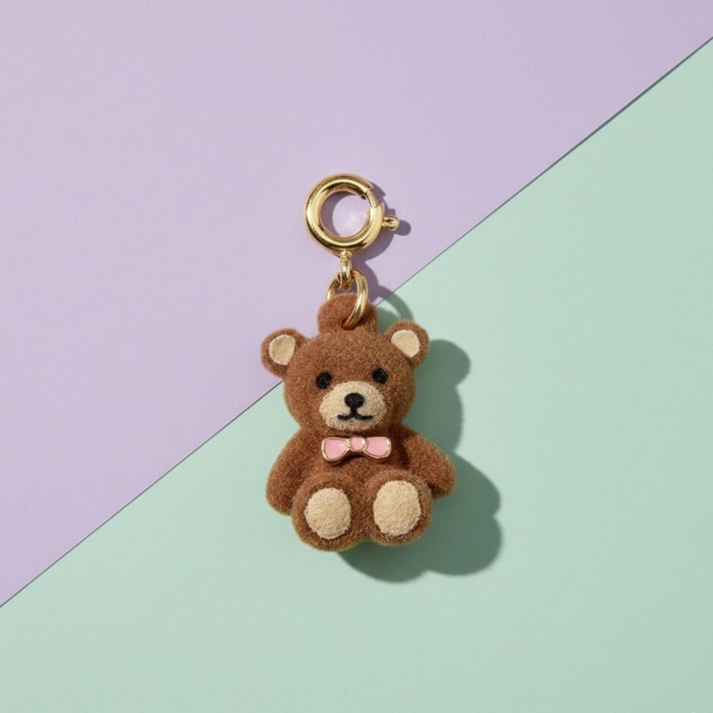 Brown teddy bear keychain with a pink bow on a two-tone purple and green background
