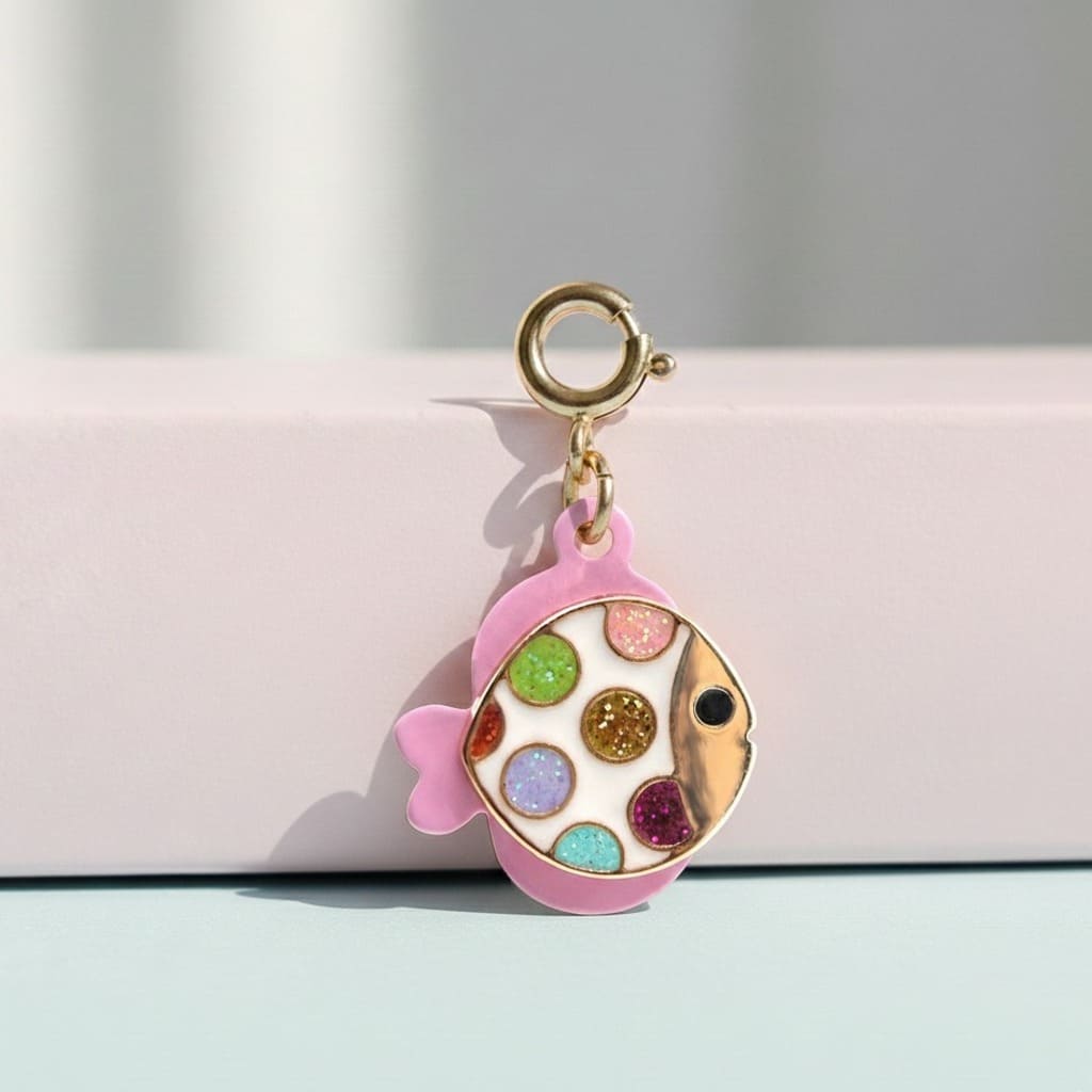 Colorful fish-shaped charm with a gold ring on a pink background