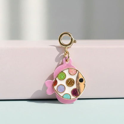 Colorful fish-shaped charm with a gold ring on a pink background