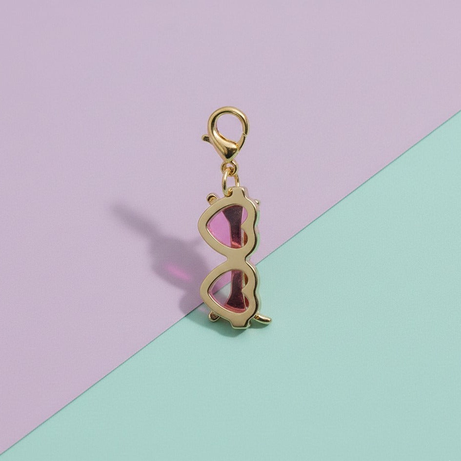 Gold sunglasses-shaped charm on a pastel pink and green background