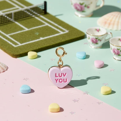 Heart-shaped charm with 'LUV YOU' text on a colorful surface with tea cups and candies.