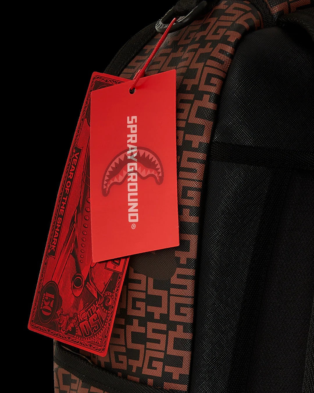 Red 'Sprayground' tag on a black backpack with a geometric pattern.