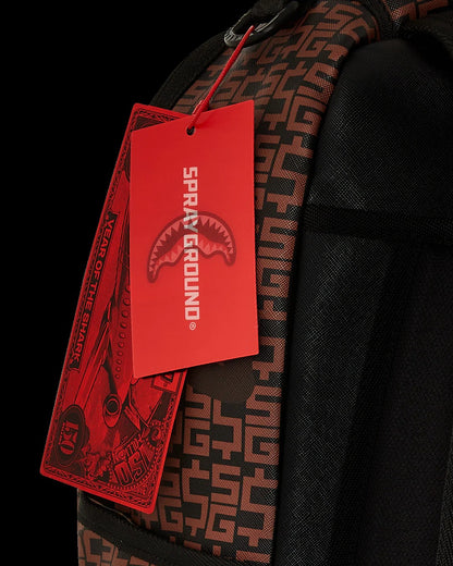 Red 'Sprayground' tag on a black backpack with a geometric pattern.