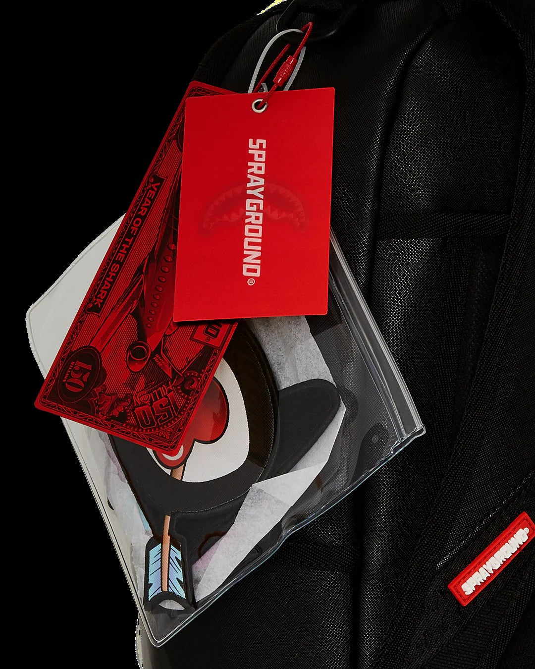 Sprayground product with red tag and clear packaging on a black background